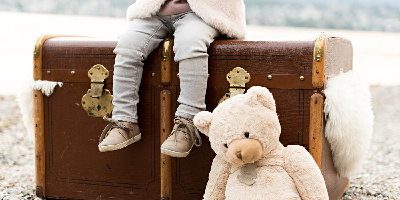 Child sitting on suitcase with teddy bear