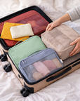 Person packing colorful packing cubes into an open suitcase on a bed.